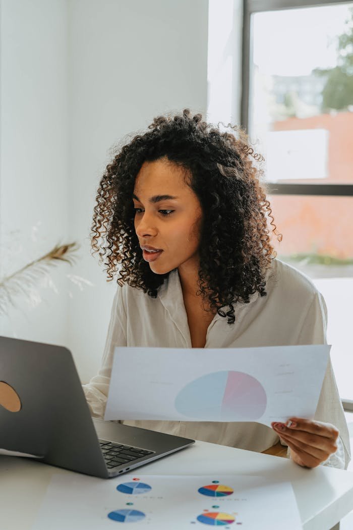 Confident woman working on a laptop, analyzing business charts in a bright office setting.